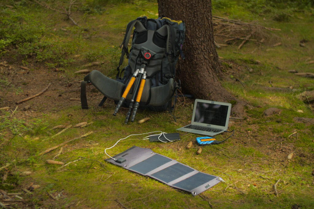 A small foldable solar panel charging a tablet and laptop. The solar panel is small enough to fit in a hiking backpack.