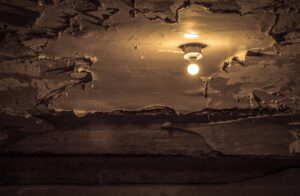 A picture of a peeling ceiling lit by a single lightbulb.