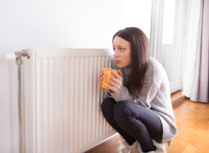 A cold woman crouching next to her HVAC unit.