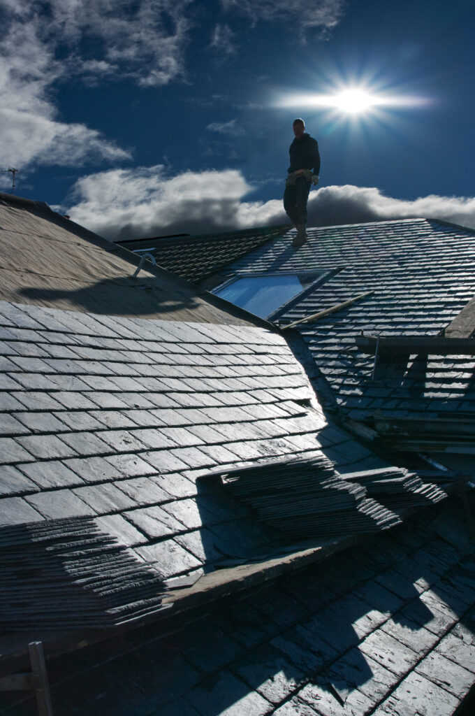 Roofing installation being done on a suburban home, roofer standing beside tiles