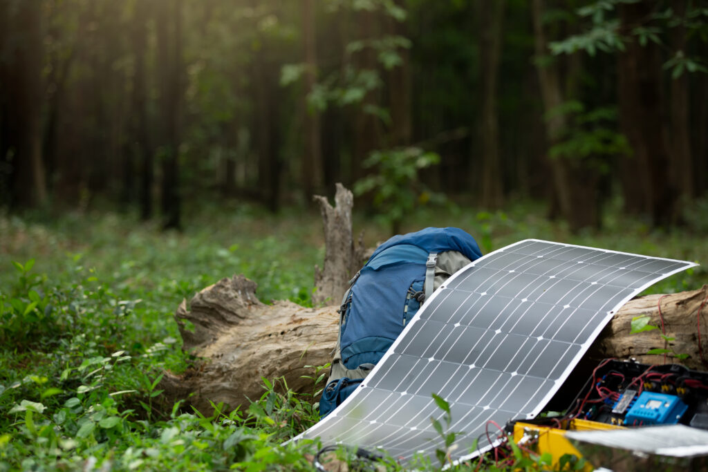 A flexible, portable solar panel next to a hiking backpack.